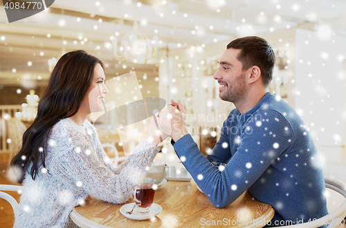 Image of happy couple with tea holding hands at restaurant