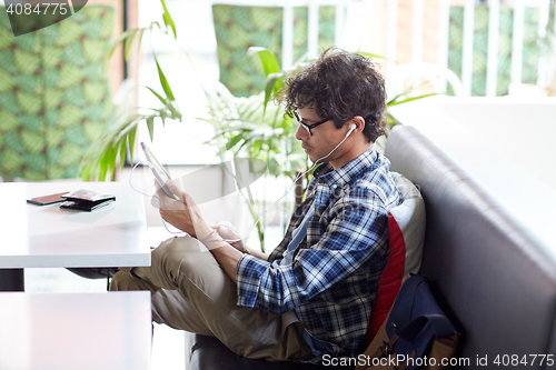 Image of man with tablet pc and earphones sitting at cafe