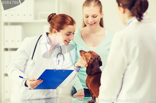 Image of happy woman with dog and doctor at vet clinic