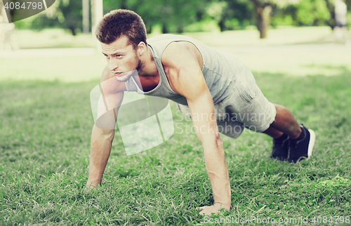 Image of young man doing push ups on grass in summer park