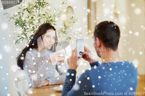 Image of man taking picture of woman by smartphone at cafe