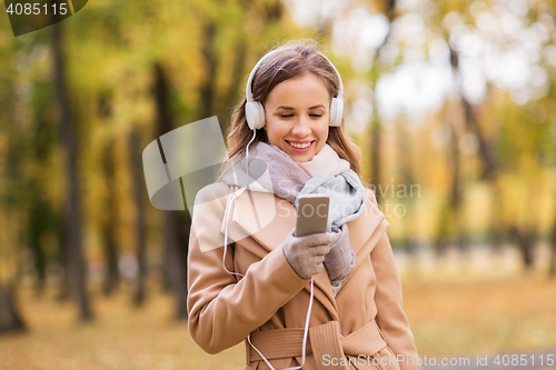 Image of woman with smartphone and earphones in autumn park
