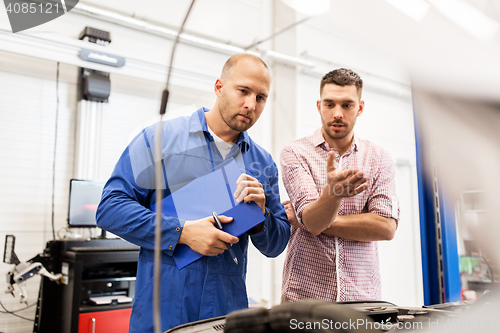 Image of auto mechanic with clipboard and man at car shop