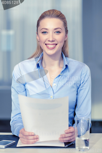 Image of smiling woman holding papers in office