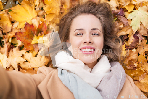 Image of beautiful happy woman lying on autumn leaves