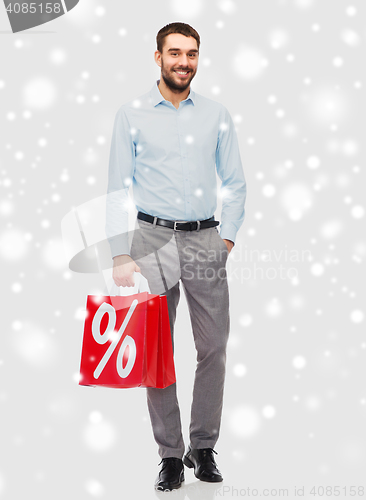 Image of smiling man with red shopping bag over snow