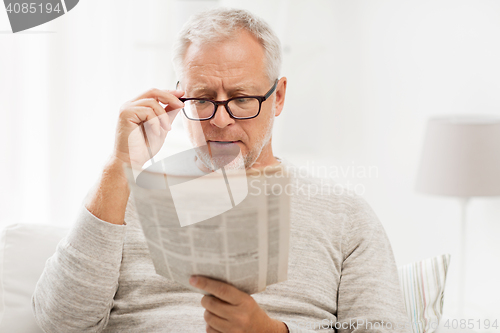Image of senior man in glasses reading newspaper at home