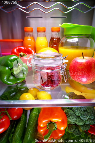 Image of Fresh raspberries in a glass jar on a shelf open refrigerator