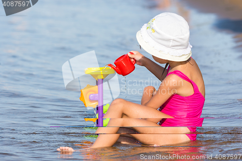 Image of Five-year girl in a pink bathing suit sitting in on the river bank and plays in the sand toys