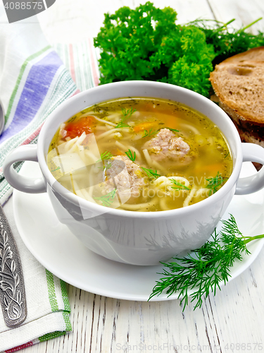 Image of Soup with meatballs and noodles in white bowl on board