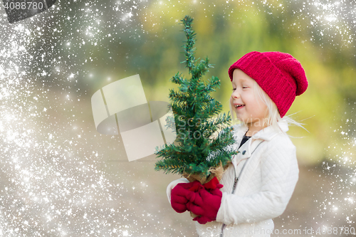 Image of Baby Girl In Mittens Holding Small Christmas Tree with Snow Effe