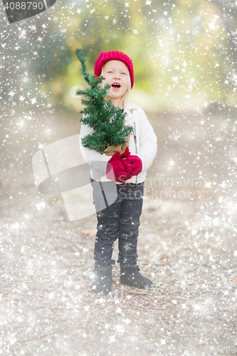 Image of Baby Girl In Mittens Holding Small Christmas Tree with Snow Effe