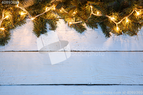 Image of Christmas wooden background with evergreen branches and golden lighted garland