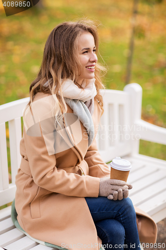 Image of happy young woman drinking coffee in autumn park