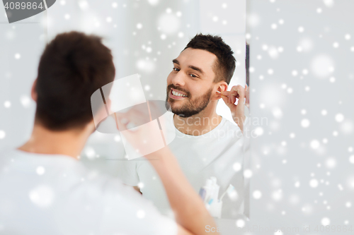 Image of man cleaning ear with cotton swab at bathroom