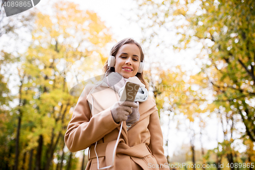 Image of woman with smartphone and earphones in autumn park