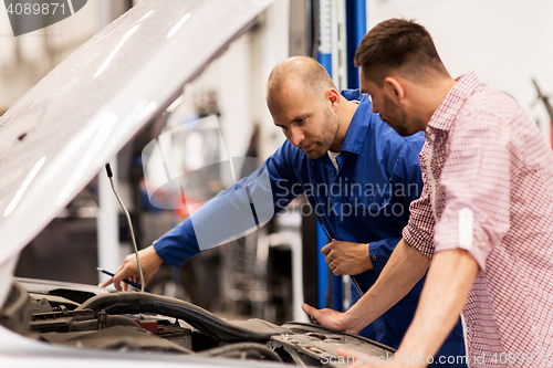 Image of auto mechanic with clipboard and man at car shop