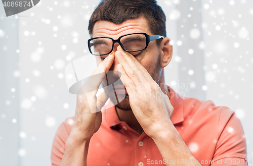 Image of tired man in eyeglasses rubbing eyes at home