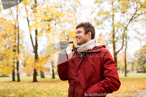 Image of man recording voice on smartphone at autumn park