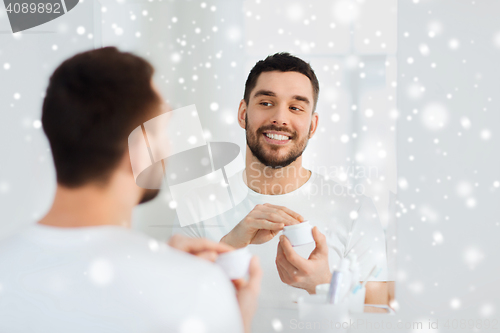 Image of happy young man applying cream to face at bathroom