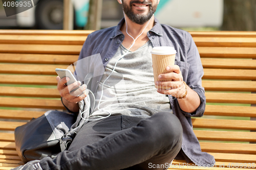 Image of man with earphones and smartphone drinking coffee