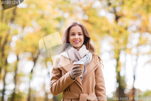 Image of happy young woman drinking coffee in autumn park