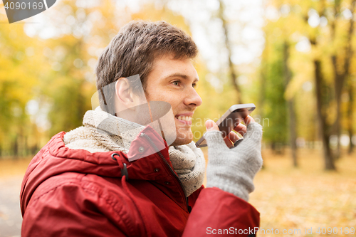 Image of man recording voice on smartphone at autumn park