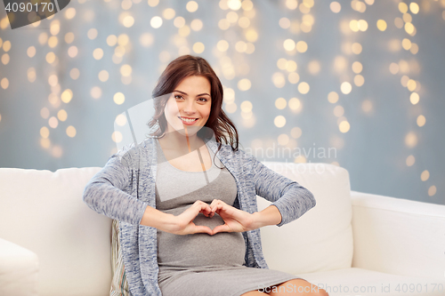 Image of happy pregnant woman making heart gesture at home