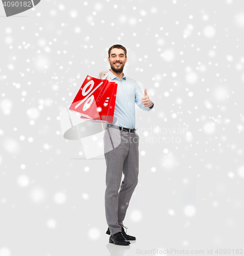 Image of smiling man with red shopping bags over snow