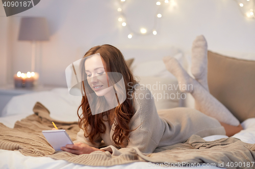 Image of happy young woman with notebook in bed at home