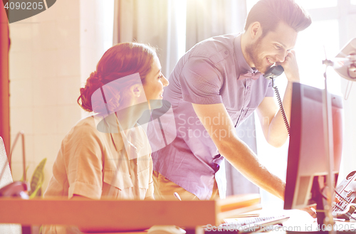 Image of happy creative team calling on phone in office