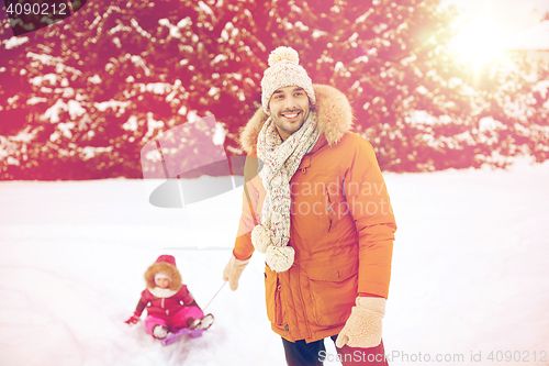 Image of happy man carrying little kid on sled in winter