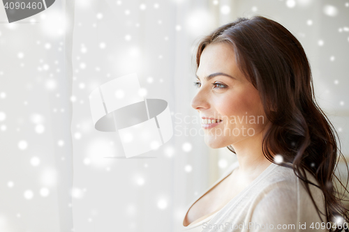 Image of happy young woman looking through window at home