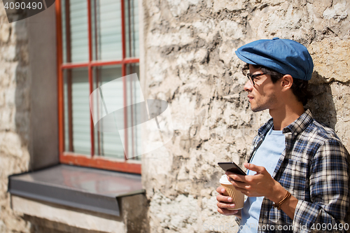 Image of man with smartphone drinking coffee on city street