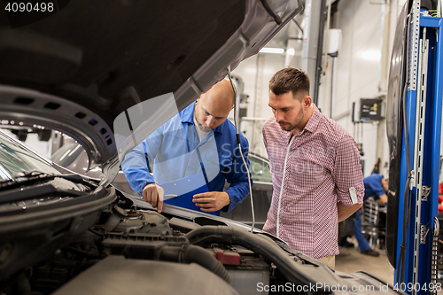 Image of auto mechanic with clipboard and man at car shop