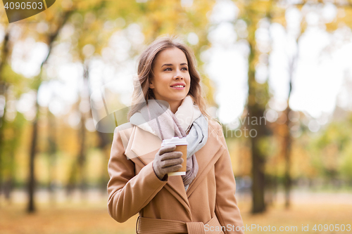 Image of happy young woman drinking coffee in autumn park