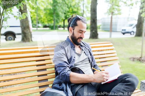 Image of man writing to notebook or diary on city street