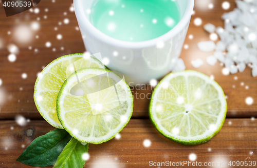 Image of citrus body lotion in cup and limes on wood