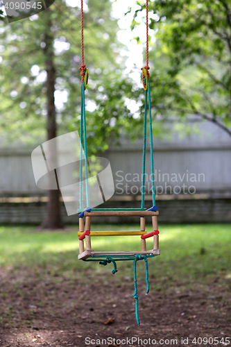 Image of empty wooden swing hanging in summer garden