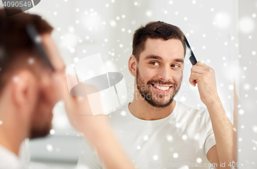 Image of happy man brushing hair with comb at bathroom