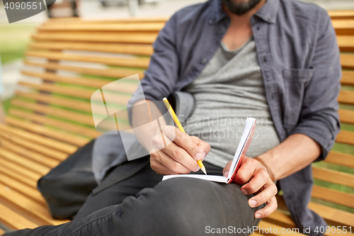 Image of close up of man writing to notebook on city street