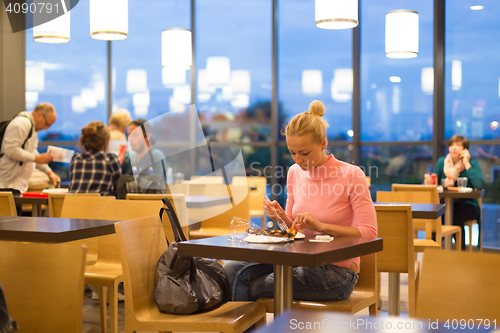 Image of Young woman eating pizza at airport restaurant while waiting for flight departure.