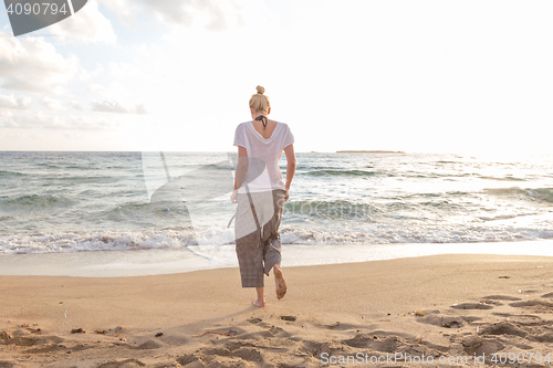 Image of Woman walking on sand beach at golden hour