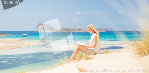 Image of Woman reading book, enjoying sun on beach.