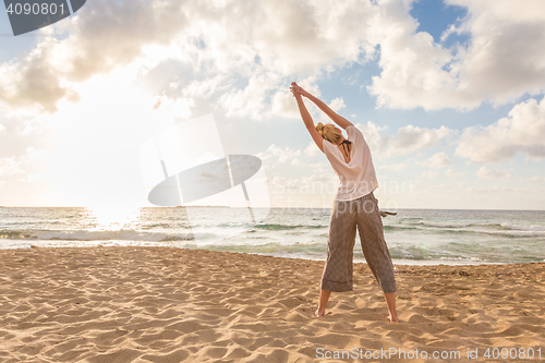 Image of Woman practicing yoga on sea beach at sunset.