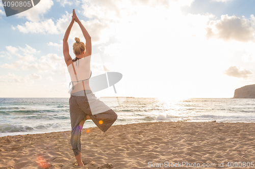 Image of Woman practicing yoga on sea beach at sunset.