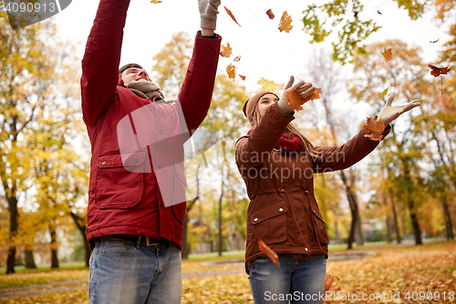 Image of happy young couple throwing autumn leaves in park