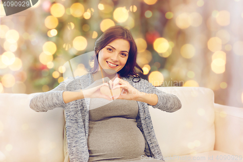 Image of happy pregnant woman making heart gesture at home