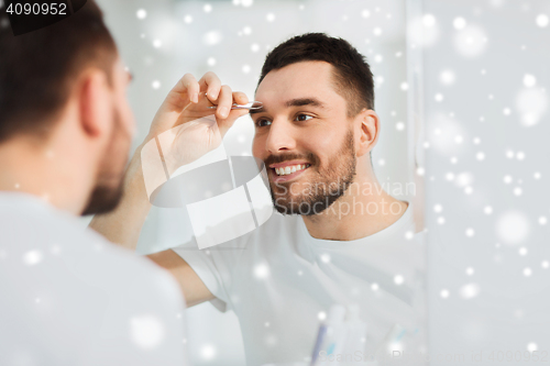 Image of man with tweezers tweezing eyebrow at bathroom