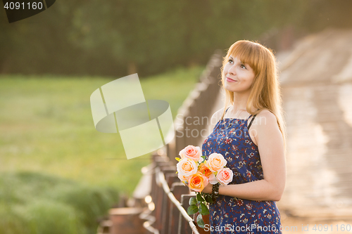 Image of Young girl with a bouquet of roses standing on the bridge in the background blurred foliage